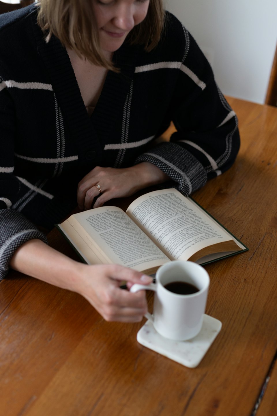 Mani che tengono un libro aperto e una tazza di caffè su un tavolo.