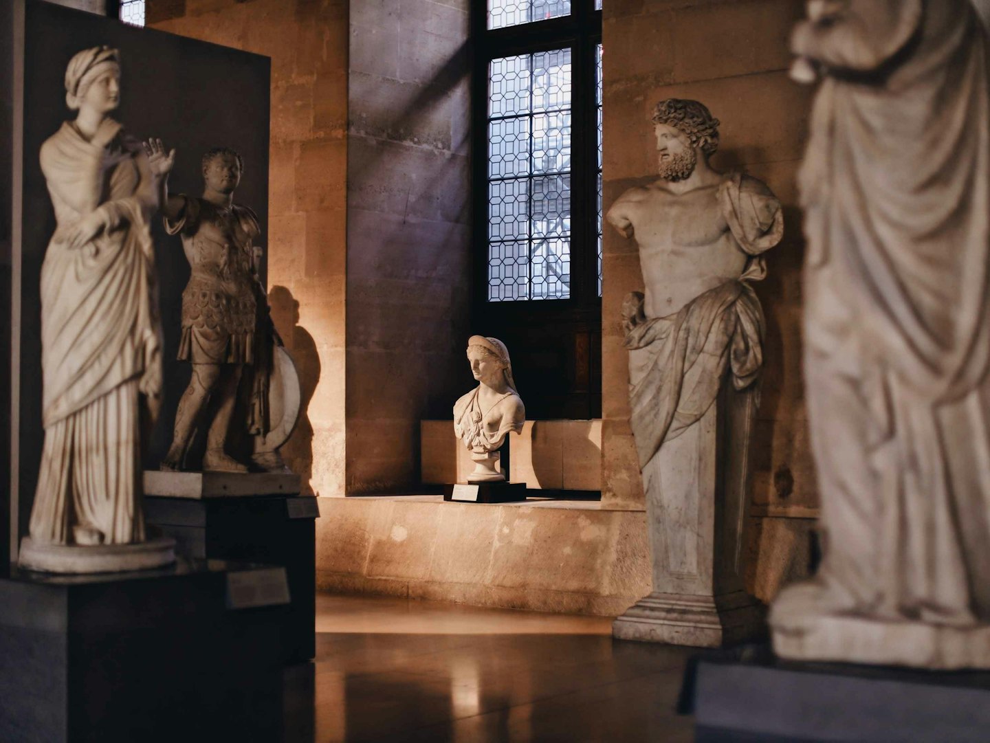 Antiche statue di marmo su piedistalli in un corridoio di museo.